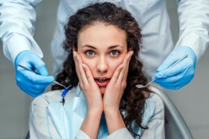 Woman with hands on her face in fear, dentist behind her with tools dental anxiety sedation dentistry dentist in Virginia Beach Virginia